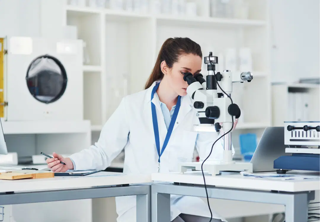 Female scientist working with a microscope in a modern laboratory, representing MedTech research, compliance, and innovation.