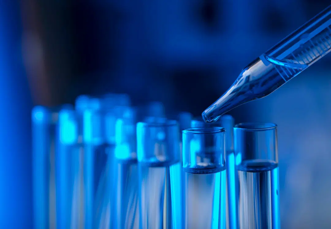 Laboratory pipette adding liquid to test tubes under blue light, symbolizing specialty chemicals, R&D, and supply chain resilience.